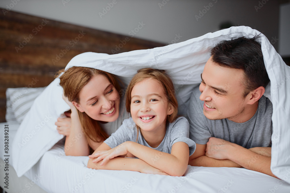portrait of positive parents and kid girl happy together at home, spending time together on bed and enjoy. leisure