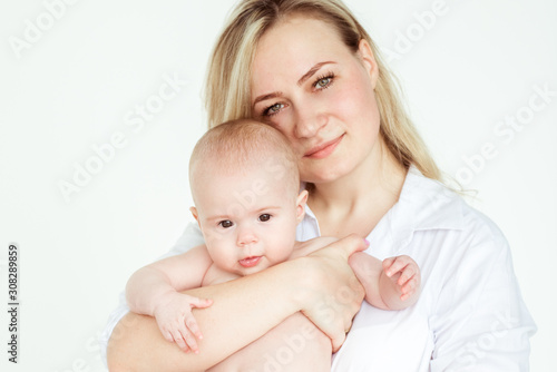 Cute infant baby on mothers hands standing in the room. Mother hugging baby with love. Happy motherhood and maternity concept