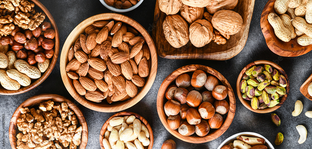 A variety of nuts in wooden bowls from top view. Walnuts, cashew, almond, pistachio, pecan, hazelnut, macadamia and peanut mix selection. Healthy fitness super food banner or panorama. A variety of nuts in wooden bowls from top view. Walnuts, cashew, almond, pistachio, pecan, hazelnut, macadamia and peanut mix selection. Healthy fitness super food banner or panorama.