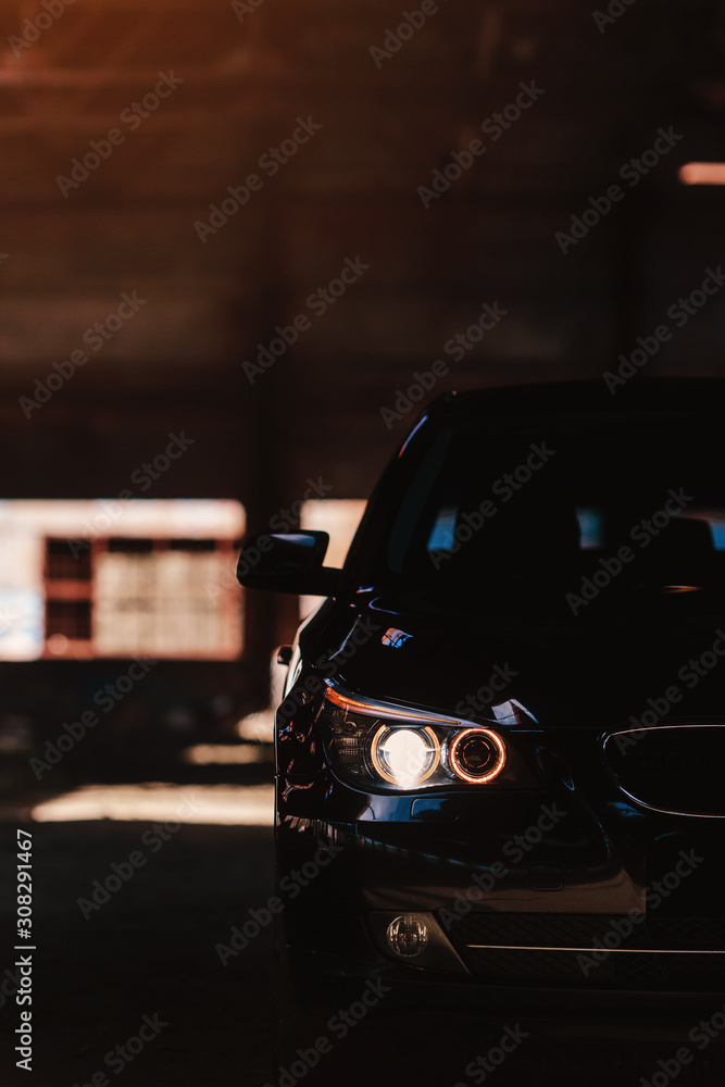 Fototapeta premium Car headlight of powerful sports black car on dark background. Car headlight at night.