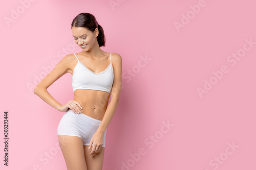 attractive charming young lady, caucasian brunette with perfect body posing isolated over pink background, portrait of female in undrwear.