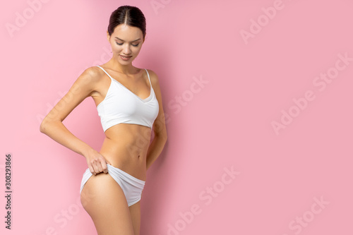 attractive charming young lady, caucasian brunette with perfect body posing isolated over pink background, portrait of female in undrwear.