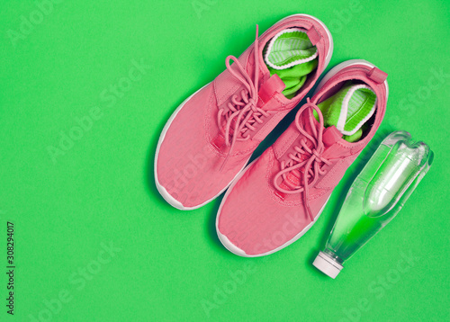 Pink sport shoes and bottle of water on a green background. Concept of healthy lifestyle, sport and diet. Text space. Top view. Flat lay. 