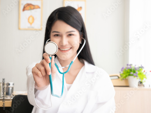 Portrait of a woman doctor and holding stethoscope in the examination room. Closeup at stethoscope. Happy beautiful doctor and smiling in hospital or clinic.