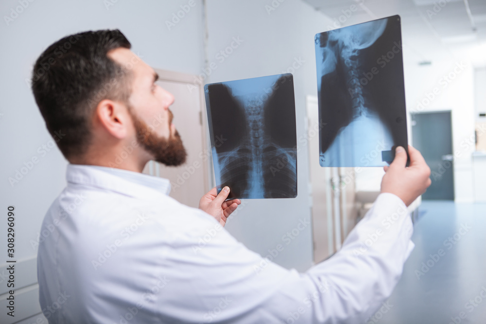 Fototapeta premium Rear view shot of a male practitioner comparing two x-ray scans of the spine of a patient