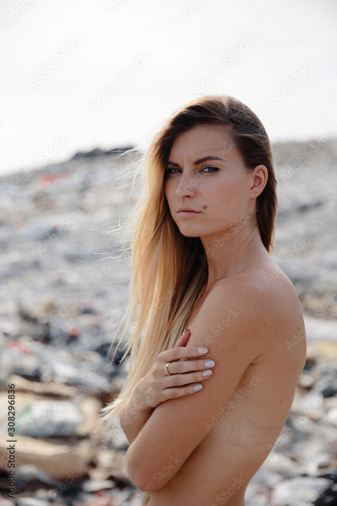 Nature pollution activist at a huge trash dump outdoors - Naked topless blonde woman - Looking at all the human waste and plastic in our world - Seagulls flying in Eastern Europe Latvia Riga