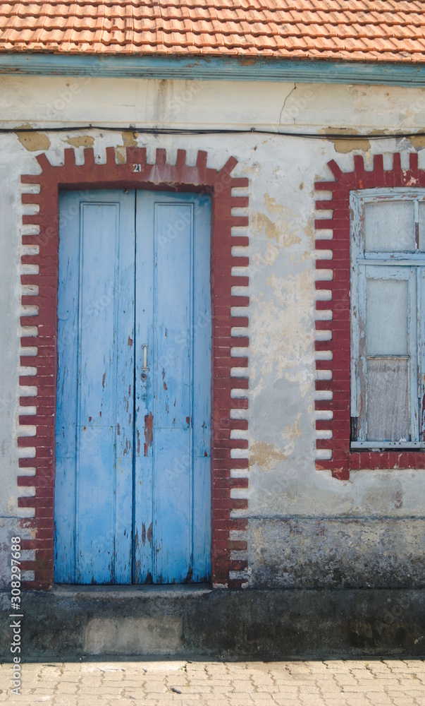 Porta e janela de uma casa velha, tipícas do sul de Portugal com tijolos em redor, contraste de vermelho branco e azul