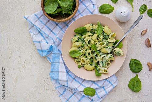 Spring green pasta with spinach and green peas in a creamy sauce in a beige clay plate on a light concrete background. Pasta Recipes. Italian food. Copyspace.