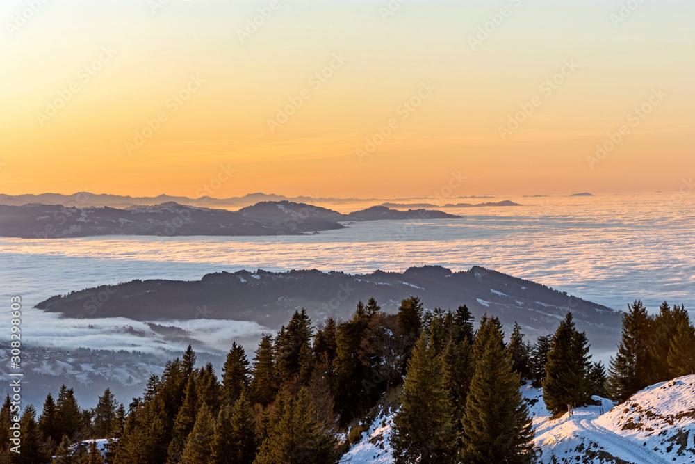 Colorful sunset in the Bregenzerwald region with snow-covered hills. Fog over the Rhine valley and the lowlands. Austria, Switzerland