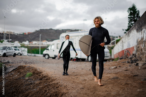 Photography Two smiling man and woman surfers with the surf boards walking to the sea shore