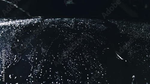 Drop flow down the hood. Close up view of a bonnet car. Dark black cinematic picture. Process stage of polishing and washing auto. Zoom camera dolly shooting. Hose is poured over cowl with water.