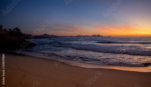 Warm colourful glowing sunrise at the crack of dawn at the Arpoador Devil s beach in Rio de Janeiro with waves coming in reflecting the orange colours of the sun and a pristine sand beach