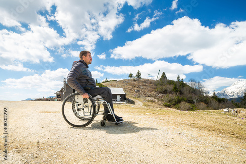 Happy man in wheelchair outside in nature on a sunny summer day in the mountains