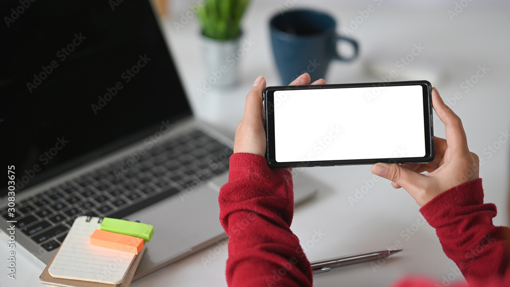 Closeup woman holding her mockup smartphone on office desk.