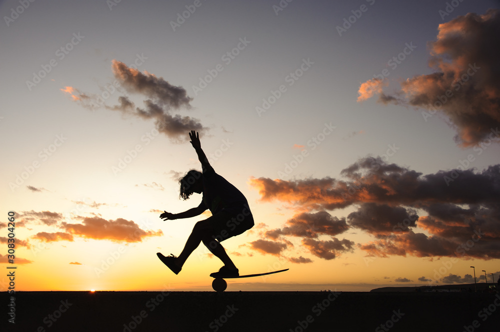 Silhouette of the man standing on the balance board on the one leg on the bending knee Silhouette of the man standing on the balance board on the one leg on the bending knee
