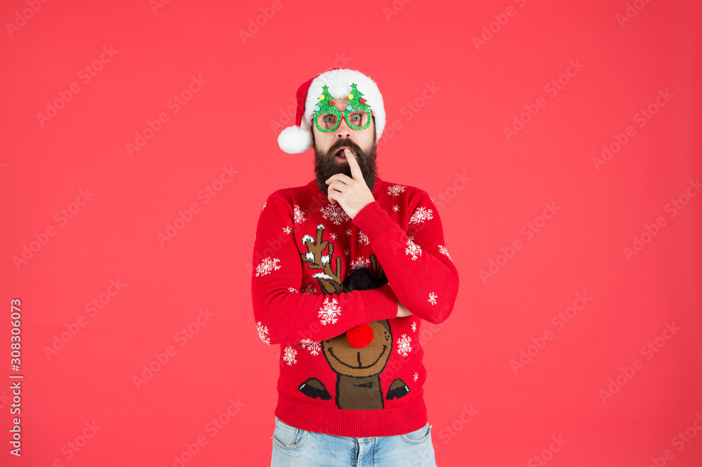 surprised male in xmas party glasses. happy new year. funny hipster knitted sweater. warm clothes for cold weather. winter holiday season. bearded man santa hat red background. merry christmas