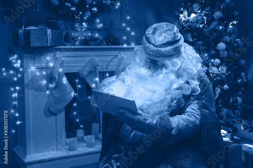 Russian Santa Claus (Grandfather Frost)  use his mobile tablet with glowing screen to choose  gifts for Christmas and New Year. Classic blue color 2020