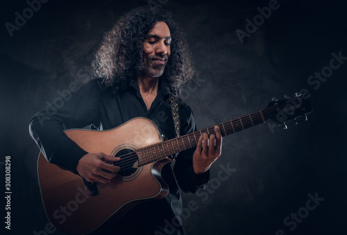 Talented musician is performing with his guitar at dark studio.