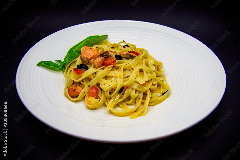 Pasta with salmon and olives on black background