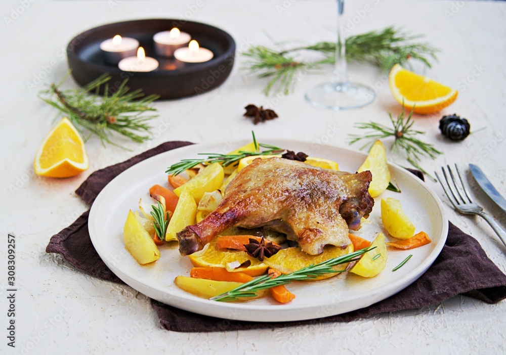 Roasted duck leg with potatoes, carrots and slices of orange on a ceramic plate on a light concrete background. Christmas and New Year dishes recipes. Duck recipes. French cuisine