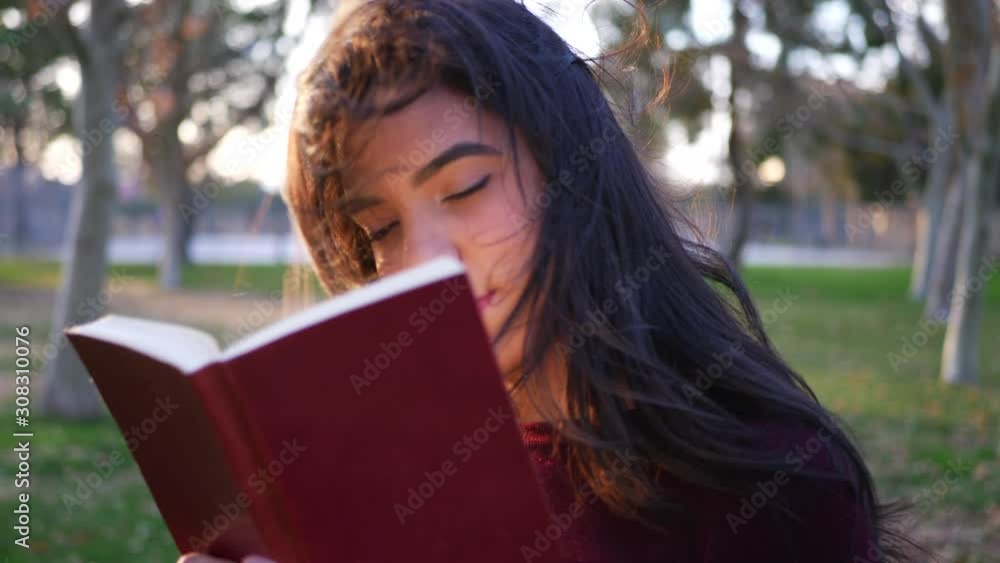 A young woman college student reading a story book outdoors in the park at sunset SLOW MOTION. A young woman college student reading a story book outdoors in the park at sunset SLOW MOTION.