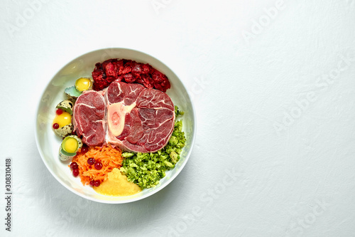 Healthy fresh dog food ingredients in a big white bowl on white background. Raw beef meat, vegetables , eggs and organs. Copy space.