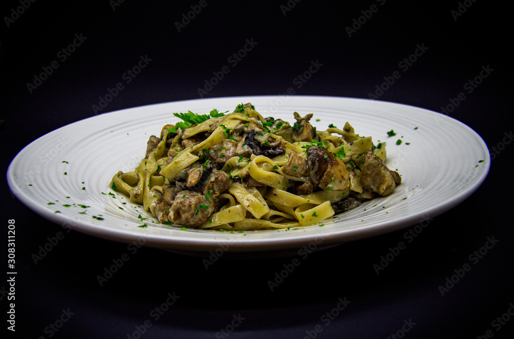 Pasta with mushrooms and pork on a black background