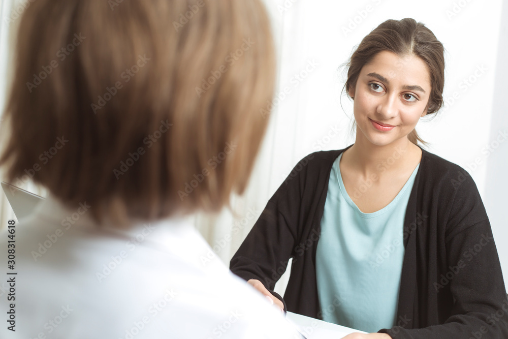 Indian friendly business woman advises a client. Two women are talking while sitting at the table. Indian friendly business woman advises a client. Two women are talking while sitting at the table.