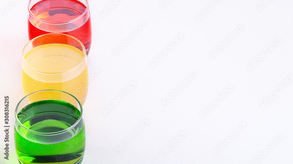 Glasses of various colors and tastes soda drink on white background. Red, yellow, green soda or sparkling water close up on white table, copy space Glasses of various colors and tastes soda drink on white background. Red, yellow, green soda or sparkling water close up on white table, copy space