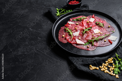 Marbled beef carpaccio with arugula and parmesan cheese. Black background. Top view. Space for text