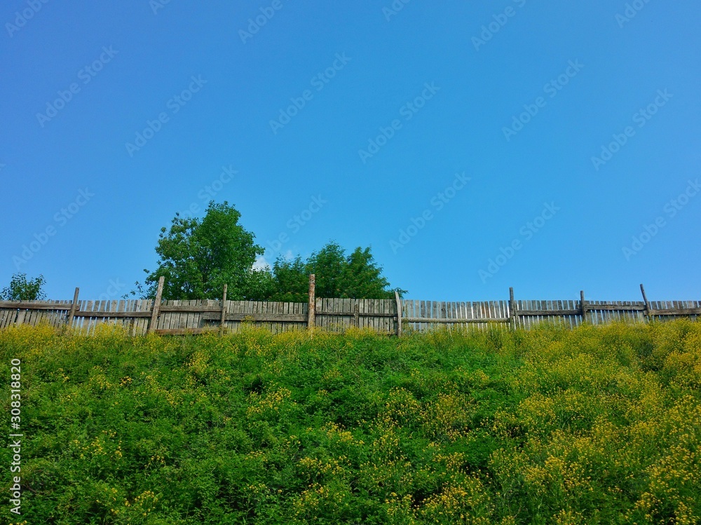 Bright landscape of green grass hill with a wooden fence on the top