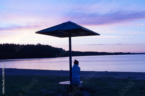 Young woman sits on a night deserted beach under a beach umbrella