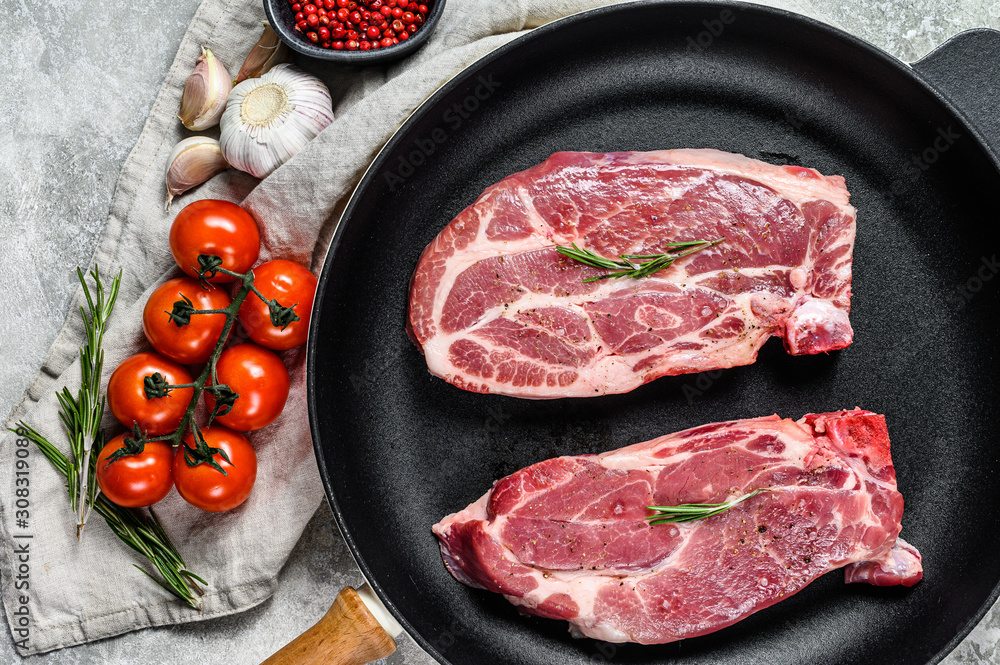 Raw pork steak in a frying pan. Marbled farm meat. Gray background. Top view