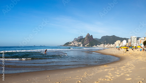 Panorama of early morning Ipanema beach in Rio de Janeiro with the ocean and footsteps on the beach in the foreground and the Two Brothers mountain in the background against a clear blue sky photo