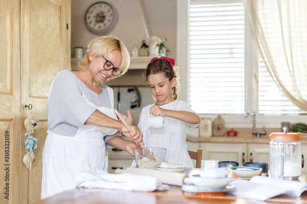 Cute little girl with her grandmother cooking together at kitchen table. Cute little girl with her grandmother cooking together at kitchen table.