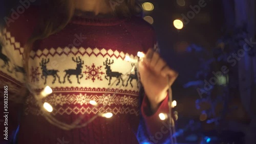 Young Cute teen girl in deer sweater dancing with luminous lanterns, flashing lights for Christmas and Happy New Year home party. Have fun. Celebrate Christmas.