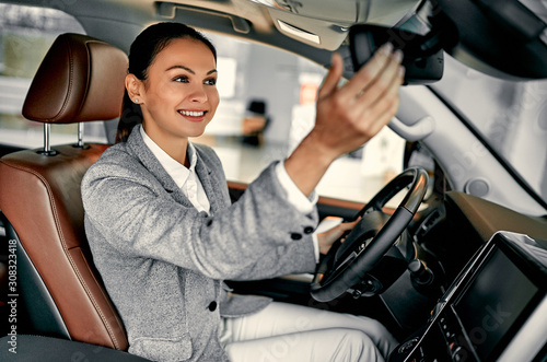 Fotografija Attractive young businesswoman is choosing new vehicle and shifting rear-view mirror in car dealership