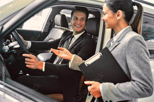 Professional salesperson during work with customer at car dealership. Successful young businessman in a suit chooses a new car.