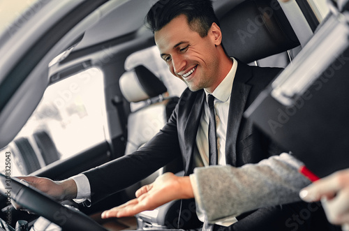 Successful young businessman in a suit chooses a new car. The seller helps to choose a car. © Valerii Apetroaiei