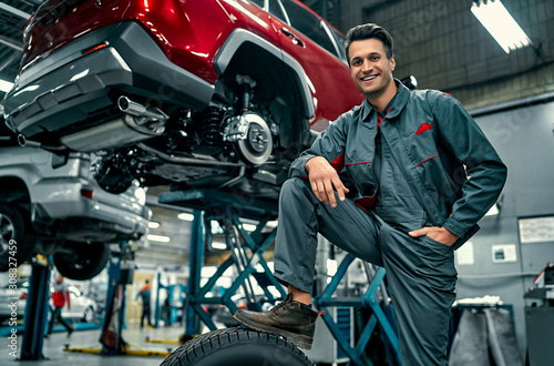 Handsome mechanic in uniform is working in auto service. Car repair and maintenance. Holding car wheel. photo