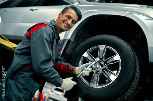 Handsome mechanic in uniform is working in auto service. Car repair and maintenance. Holding car wheel.