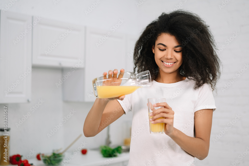 Young beautiful African American woman holding glass with an orange juice. Healthy lifestyle concept, natural organic breakfast at kitchen Young beautiful African American woman holding glass with an orange juice. Healthy lifestyle concept, natural organic breakfast at kitchen