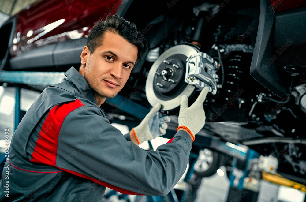 Car mechanic worker repairing suspension of lifted automobile at auto repair garage shop station Car mechanic worker repairing suspension of lifted automobile at auto repair garage shop station
