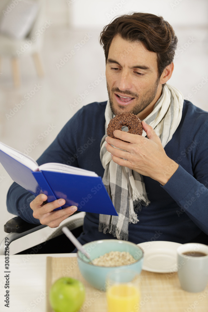 man in wheelchair reading book and eating chocolate donut man in wheelchair reading book and eating chocolate donut