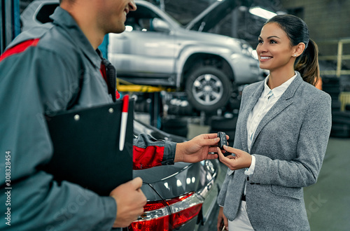 Beautiful businesswoman and auto service mechanic are discussing the work and giving keys. Car repair and maintenance. © Valerii Apetroaiei