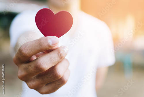 Asian man hold red heart shaped wooden piece with blur background