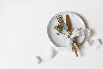 Festive table setting. Golden cutlery, berry eucalyptus branch, porcelain plate and silk ribbon isolated on white table background. Mediterranean wedding or restaurant menu concept. Flat lay, top view