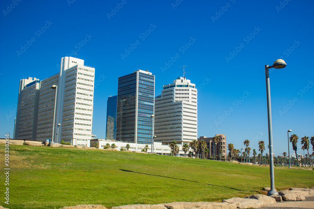 summer time Tel Aviv Israeli capital city landmark urban photography with green grass square street lantern foreground and skyscraper buildings clear blue sky background 