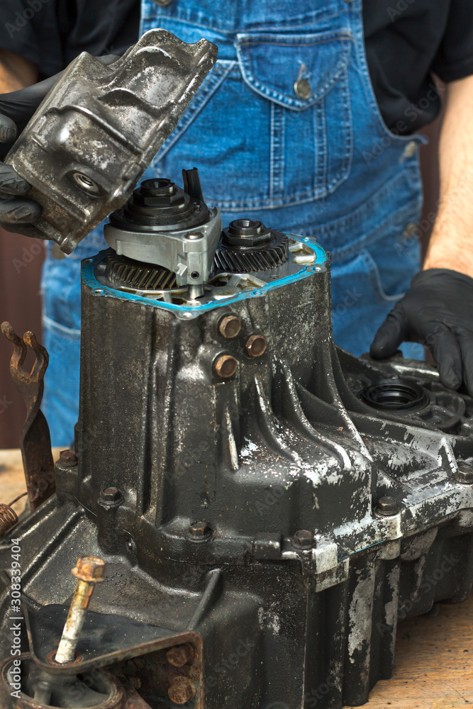 Mechanik samochodowy rozkręca manualną skrzynię biegów. Zdejmuje aluminiową pokrywę ze skrzyni biegów.
