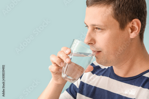 Portrait of handsome man drinking fresh water on color background
